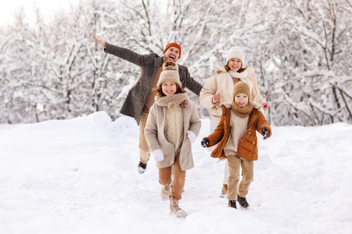 Happy kids have fun with parents outdoors in winter park, running with outstretched arms and laughing, rejoicing snowy weather, family enjoy outdoor activities during New Year and Christmas holidays